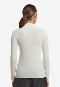 Ribbad polokragetröja i off-white stickad tyg. Åtsittande design med långa ärmar och subtil textur vid kragen och manschetterna.