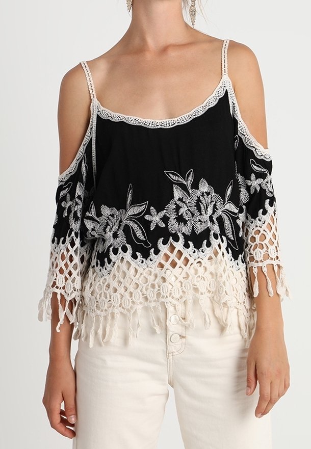 Haut noir à épaules dénudées avec broderie florale blanche, bordure en dentelle et motif crocheté à l'ourlet, avec des détails à franges.