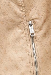 Μπεζ καπιτονέ δερμάτινο ύφασμα με ανάγλυφο λουλουδένιο σχέδιο και κοντινή λήψη ενός ασημένιου μεταλλικού φερμουάρ με χαρακτικό το "GUESS".