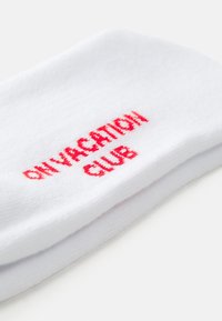 Baltos medvilninės kojinės su raudonu užrašu "VACATION CLUB". Minkšta tekstūra ir klasikinis vamzdelio dizainas.