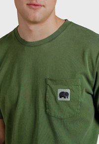 Zelené bavlněné tričko s kulatým výstřihem, které má přední kapsu s šedým prošitím a černou grafikou slona.