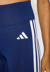 Les leggings de sport bleu marine présentent des accents blancs à trois bandes sur les côtés et un logo Adidas blanc. Confectionnés dans un tissu extensible et lisse.