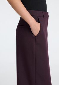 Kalhoty s vysokým pasem, tailored střihu v hluboké burgundské barvě. Mají postranní kapsy, rovný střih nohavic a hladkou texturu bez vzorů.