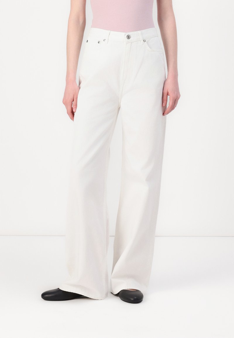 Jean large blanc en denim, avec une taille haute, coupe droite, design à cinq poches et chaussures noires.
