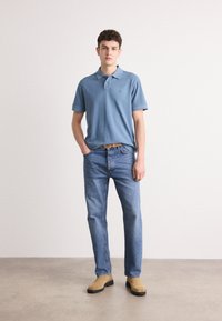 Cămașă polo de culoare albastru deschis cu guler, pereche de blugi drepți cu spălare medie și bocanci bej până la gleznă. Design simplu, accente minime.