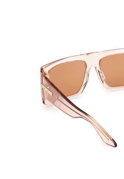 Pink-tinted oversized sunglasses with a geometric frame, brown lenses, and gold logo accent on the side. Transparent plastic material.
