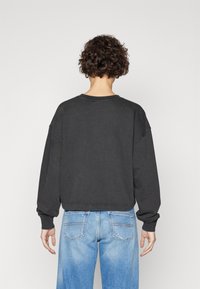 Zwarte katoenen sweatshirt met verlaagde schouders, ribgebreid mouwen en een afgeronde zoom, gedragen met lichtblauwe denim jeans met achterzakken.