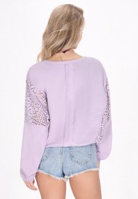 Lila trui met lange mouwen, voorzien van kantaccenten op de schouders. Geribbelde achterkant met een rechte naad, gecombineerd met denim shorts.