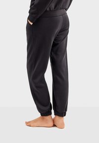 Sorte joggerbukser lavet af blødt stof. Har elastisk talje og mansjetter. Sidetasker er synlige. Ingen tydelige mønstre eller udsmykninger.