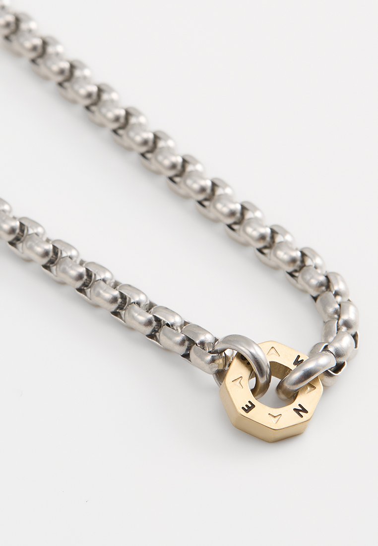 Silberne Kettenhalskette mit runden Gliedern, abgeschlossen mit einem Messing-Sechseckverschluss, der mit Richtungsschriften versehen ist.