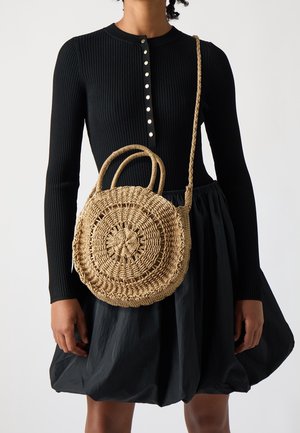 Runde geflochtene Strohtasche mit einem strukturierten, kreisförmigen Design. Verfügt über zwei Griffe und einen langen, geflochtenen Schulterriemen. Farbe: natürliches Tan.
