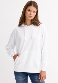 Sudadera blanca con capucha de tejido suave, que cuenta con un bolsillo tipo canguro, puños acanalados y un corte relajado. Textura lisa, diseño sencillo.