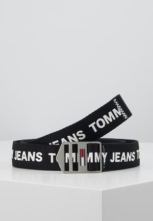 Sort stofbælte med hvid "Tommy Jeans"-tekst og en sølvspænde med røde, hvide og blå striber, vist sammenrullet på en hvid overflade.