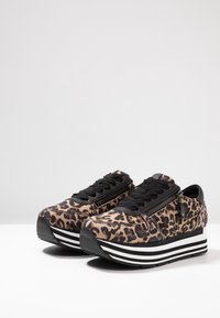 Trampki w panterkę z czarnymi sznurówkami, bocznym zamkiem błyskawicznym i koturnową podeszwą z białymi i czarnymi paskami. Wierzch wykonany z materiału, a podeszwa z gumy.