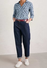 Niebieska kwiatowa bluzka z kołnierzykiem, połączona z ciemnoniebieskimi spodniami w tapered i czerwoną paskiem. Białe trampki dopełniają stylizację.