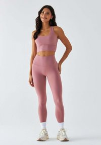 Różowy sportowy biustonosz i legginsy z wysokim stanem wykonane z elastycznego materiału. Charakteryzują się smukłym designem i teksturowanymi akcentami, zestawione z butami sportowymi.