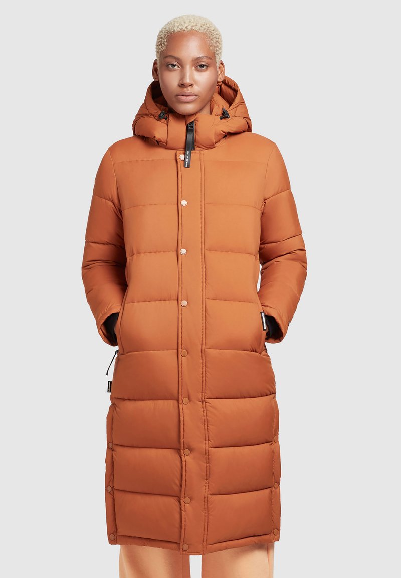 Rostfarbene Steppjacke mit Kapuze, diagonal genähten Abschnitten, Druckknöpfen und seitlichen Taschen. Weicher, texturierter Stoff.