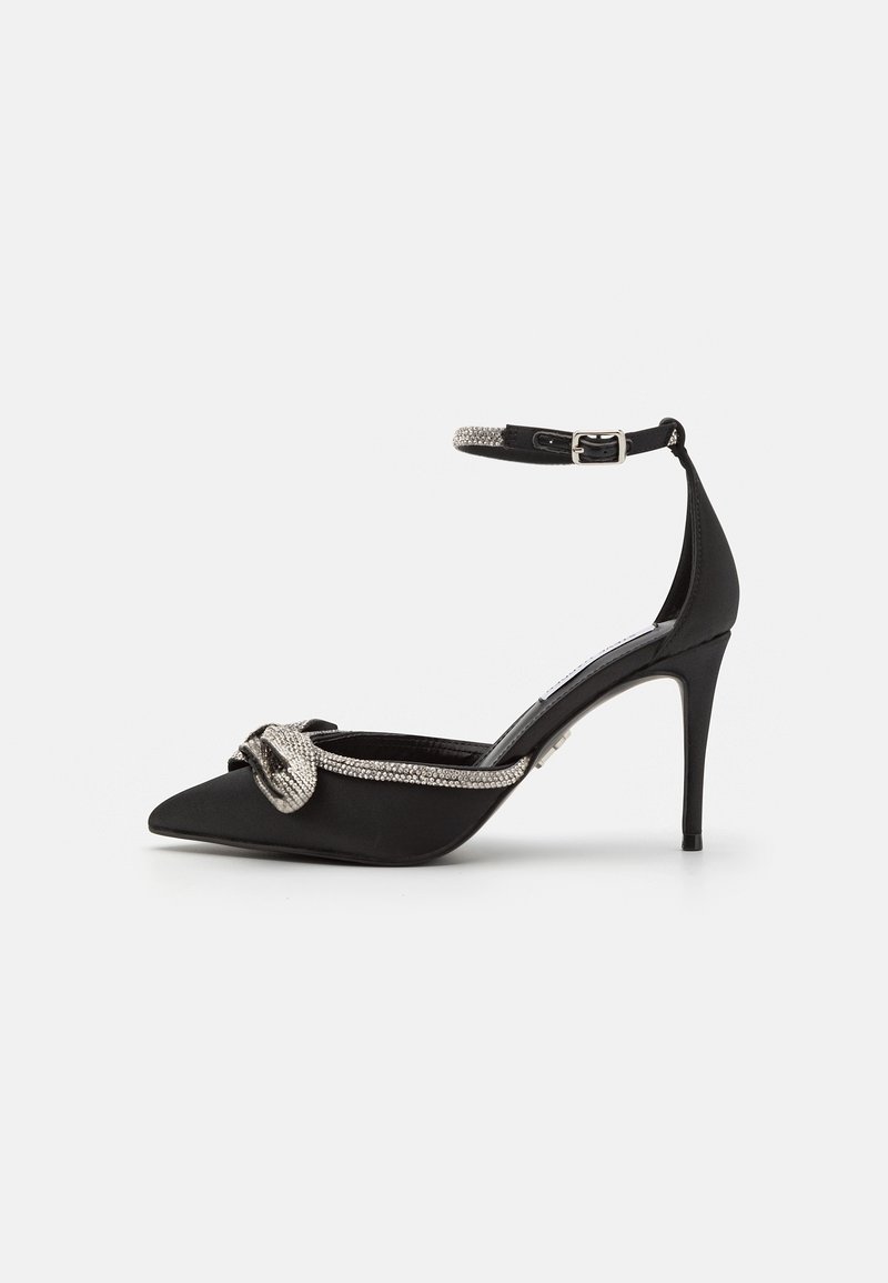 Chaussure noire à talon haut pointu avec bride à la cheville et ornement nœud en strass argenté sur l'avant.