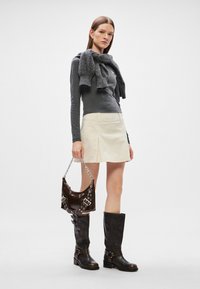 Γκρι μπλούζα με μακριά μανίκια, κρεμ μίνι φούστα, γκρι κασκόλ, καφέ γυαλιστερή τσάντα χειρός με αλυσίδα, μαύρες μπότες μέχρι το γόνατο με αγκράφες και ογκώδεις τακούνια.