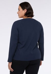 Námořnická modrá dlouhá mikina s kulatým výstřihem a přiléhavým střihem, vyrobená z měkkého materiálu. Obsahuje švy viditelné na ramenou a zádech.