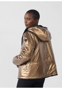 Chaqueta acolchada metálica bronce con capucha, que cuenta con un suave forro negro, cierre con cremallera y un parche redondo negro con el logo en la manga.