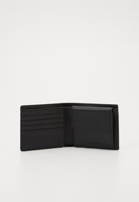 Portefeuille en cuir noir au design ouvert, doté de plusieurs emplacements pour cartes et d'un compartiment avec rabat. Texture lisse, style minimaliste.