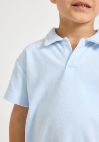Jasnoniebieska koszulka polo dla dzieci, wykonana z miękkiego materiału o fakturowanym wykończeniu, z klasycznym kołnierzykiem i krótkimi rękawami.