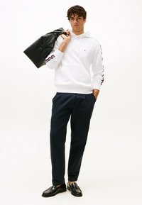 Sudadera blanca con rayas rojas y marinas, pantalones marinos y mocasines negros. Sosteniendo un bolso negro texturizado. Diseño simple con un corte relajado.