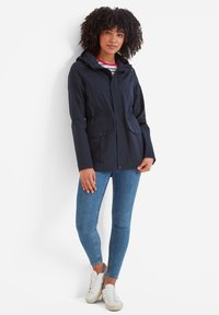 Navy rain jacket with a hood, dual front pockets, and a button closure. Paired with blue skinny jeans and white sneakers. Smooth texture.