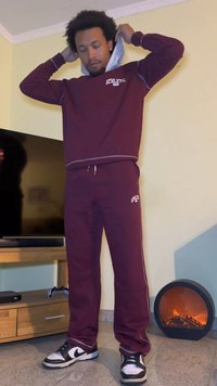 Maroon athletic sweatshirt with gray trim and matching sweatpants. Black and white sneakers. Person adjusting the sweatshirt hood.