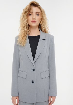 Grauer maßgeschneiderter Blazer mit zwei Vordertaschen, Reverskragen und schwarzen Knöpfen. Glatter Stoff mit einer strukturierten Passform und langen Ärmeln.