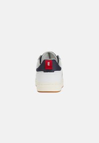 Sneaker bianca con tacco blu navy e etichetta rossa, con suola testurizzata e parte superiore in pelle liscia. Design semplice e a profilo basso.