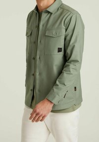 Lichtgroene button-up overhemd met twee borstzakken, schouderpas en contrasterend logo-opdruk. Gladde textuur, casual pasvorm en lange mouwen.