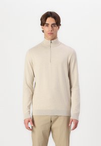 Suéter beige de cuello alto con media cremallera, puños y dobladillo acanalados, hecho de un material suave. Diseño sencillo y ajustado, sin patrones.