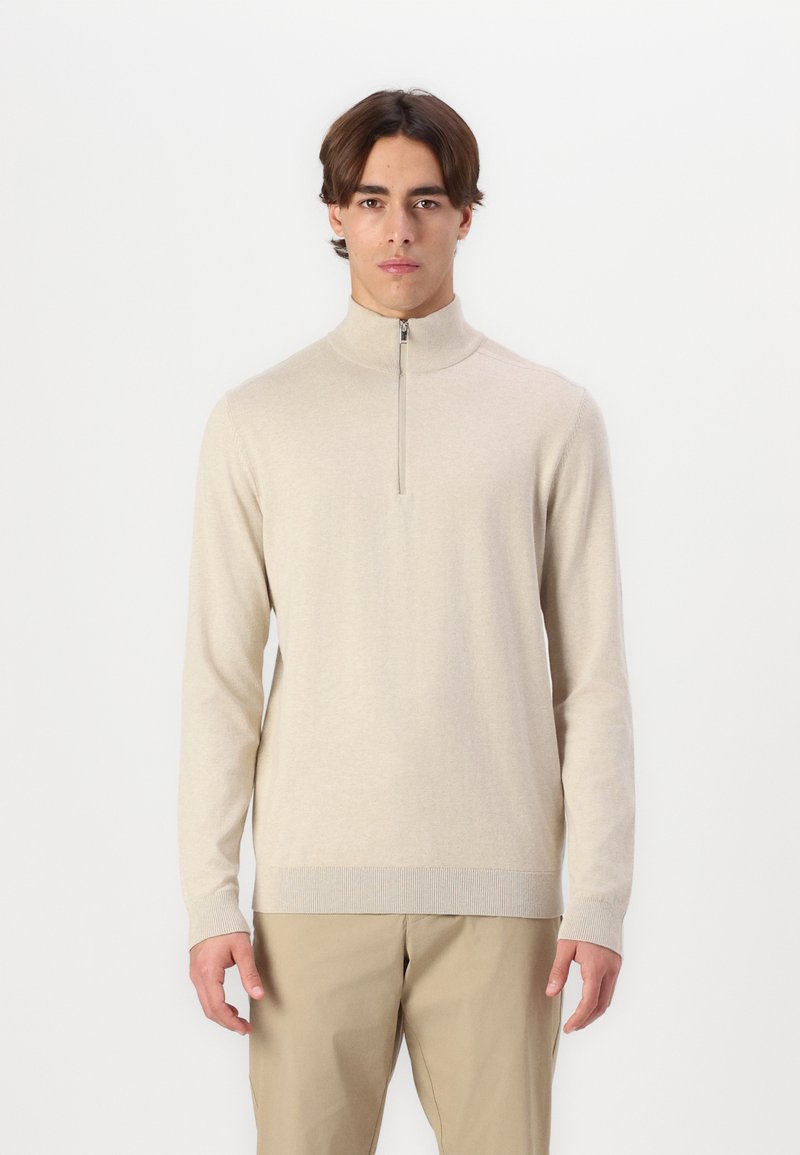 Suéter beige de cuello alto con media cremallera, puños y dobladillo acanalados, hecho de un material suave. Diseño sencillo y ajustado, sin patrones.