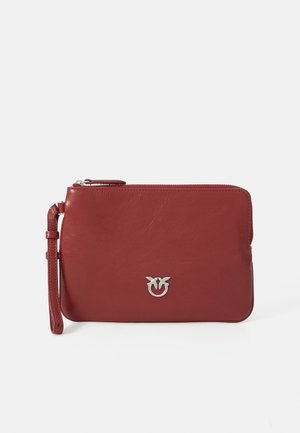 Pochette en cuir rouge avec fermeture éclair, sangle de poignet et accent en logo argenté sur le devant. Texture lisse avec un design minimaliste.