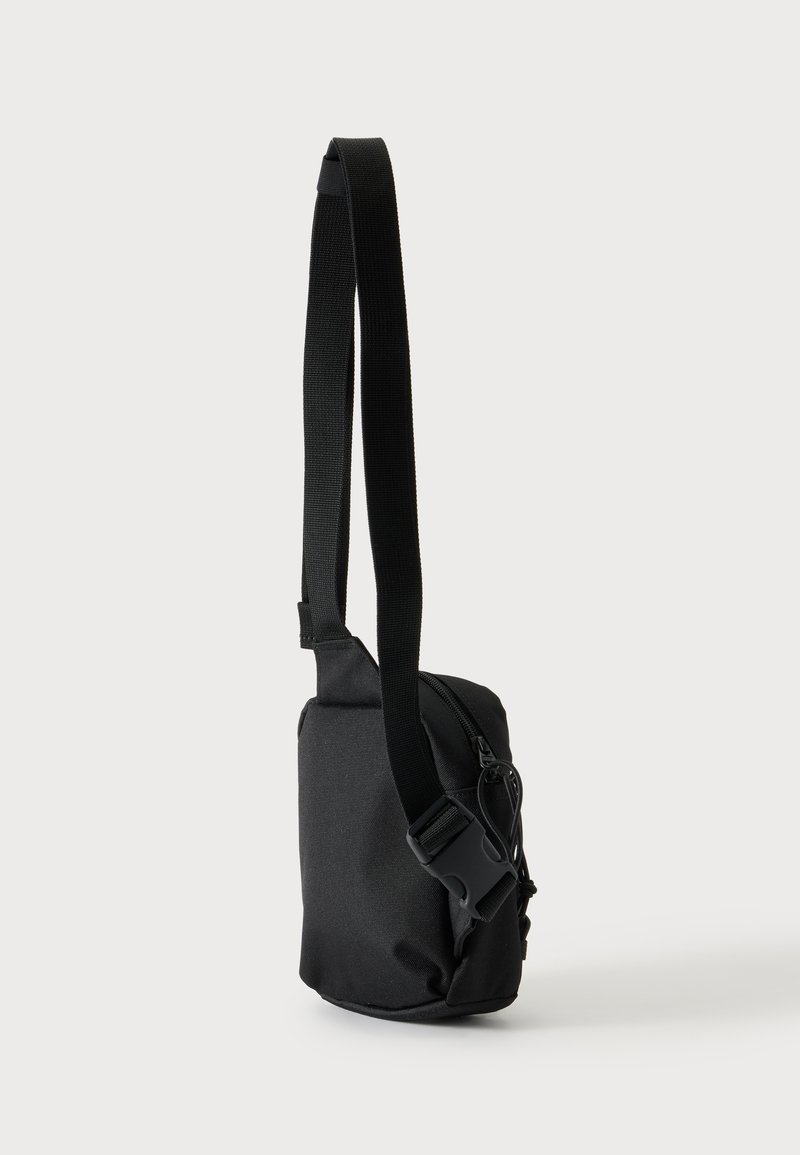 Small black crossbody bag with adjustable strap and zipper closure, shown upright against a plain light background.