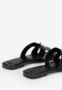 Sandali neri con una suola piatta e slanciata. Presentano due cinturini curvi sulla parte superiore, realizzati in materiale liscio. Design minimalista senza decorazioni.