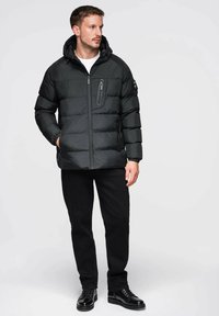 Schwarze wattierte Isolationsjacke mit Reißverschluss, Kapuze und Seitentaschen. Verfügt über gestepptes Polster und eine kleine Reißverschlusstasche auf der Brust.