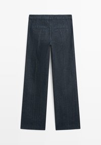 Dunkle Denimhosen mit weitem Bein. Verfügen über dezente Regenbogenstiche entlang der Nähte und zwei Gesäßtaschen.