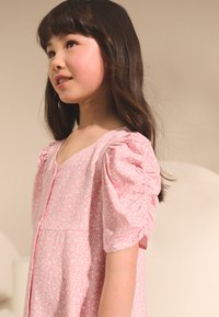 Rosa klänning med puffärm, blommönster, mjuk textur och knappar framtill. Halsringningen är rundad och tyget verkar vara lätt.