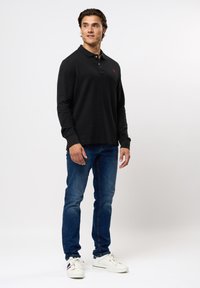 Langermet svart polo-skjorte med krage, med en rød logo. Kombinert med blå jeans og hvite sneakers. Glatt tekstur, avslappet passform.