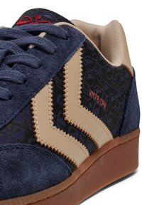 Mocka- och lädersneakers med marinblå ovansida, beige detaljer och blommönster på sidan. Utrustad med texturerade snörningar och gummisula.