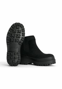 Mustat nilkkurit, joissa on kestävä kumipohja, jossa on teksturoitu pito, joustavat sivupaneelit ja pehmeä mokkajalka.
