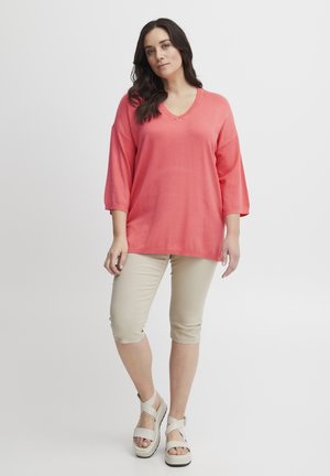 Coral V-neck top with loose fit and three-quarter sleeves, paired with beige capri pants and light-colored platform sandals.