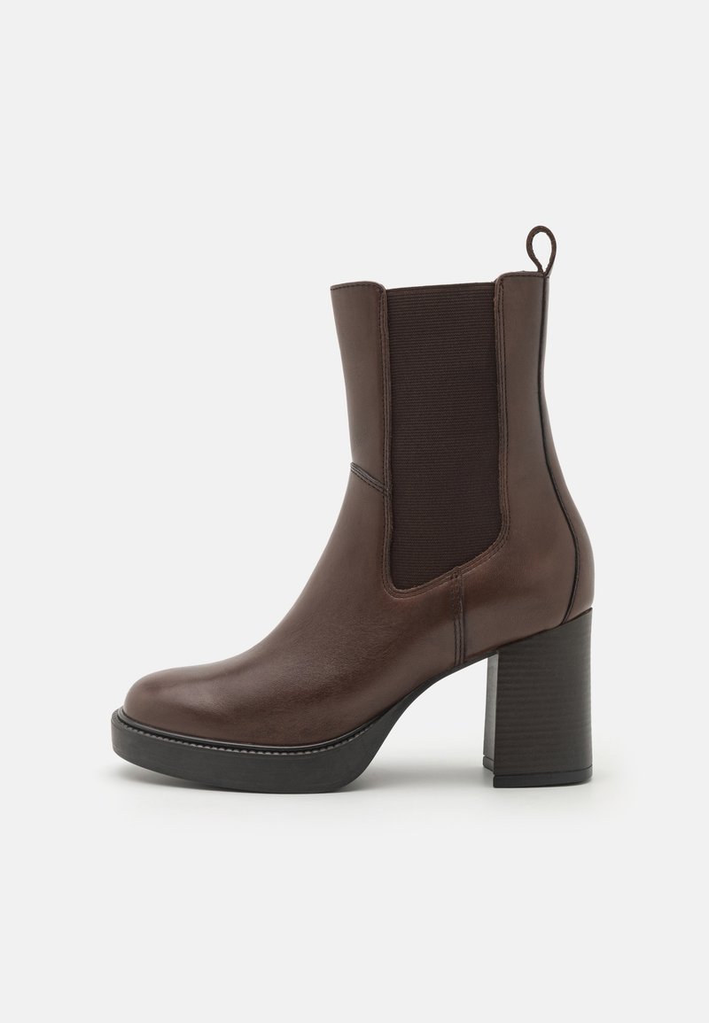Botte cheville en cuir marron avec panneau élastique latéral, languette de tirage, talon bloc épais et semelle noire sur fond blanc.