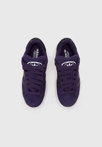 Baskets en suede violet avec des accents noirs, dotées de lacets et d'une semelle en caoutchouc. Le design inclut trois rayures sur les côtés et des logos.