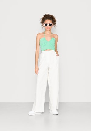 Top cropped verde-menta com alças spaghetti, combinado com calças brancas de perna larga de cintura alta e sapatilhas brancas. Design minimalista.