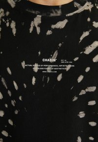 Černobílé tričko s tie-dye efektem a bílým textem "CHASIN' EST. 92," sloganem a URL webové stránky umístěné na hrudi.