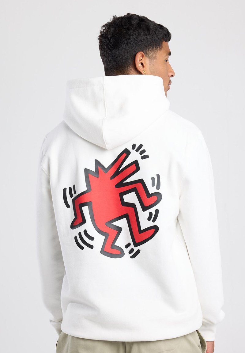 Sudadera blanca de algodón, con un gran diseño gráfico rojo y negro en la parte posterior. El diseño representa una figura abstracta en movimiento.